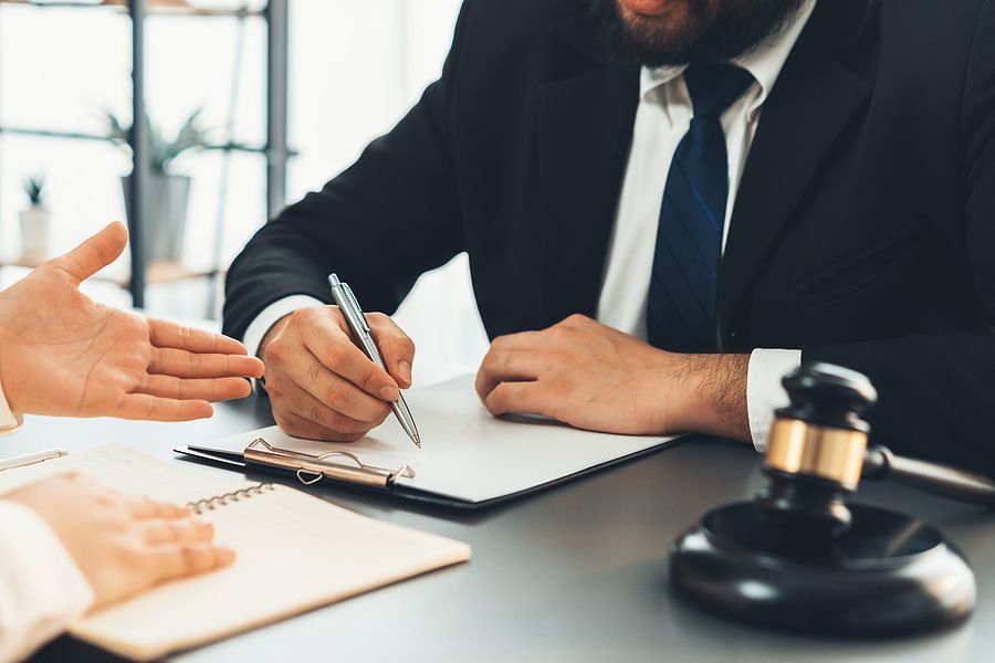 A man in a suit and tie is sitting at a table writing on a clipboard.