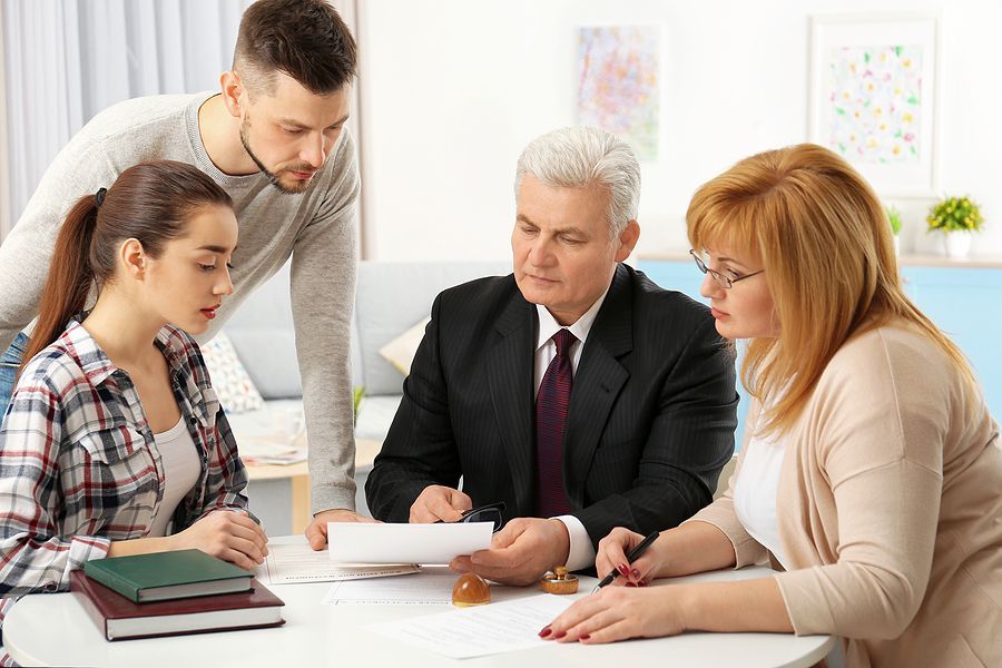 A group of people are sitting around a table with a man in a suit.