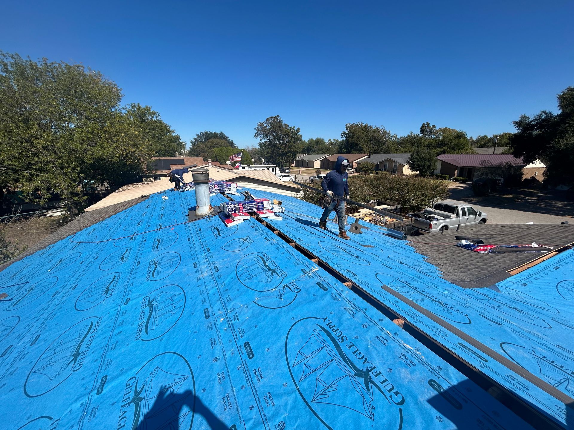 A man is standing on top of a blue tarp on a roof.