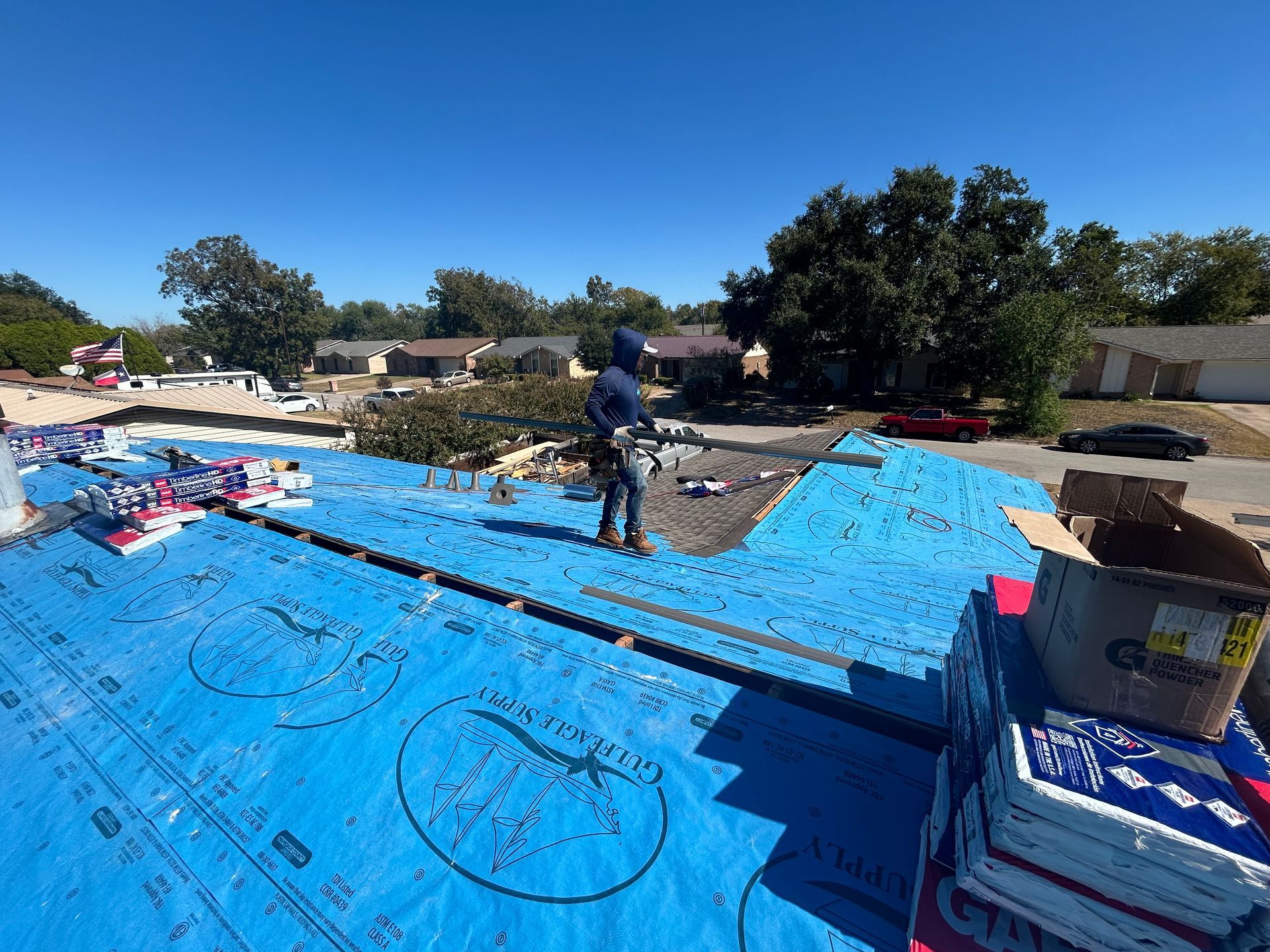 A man is standing on top of a blue tarp on a roof.