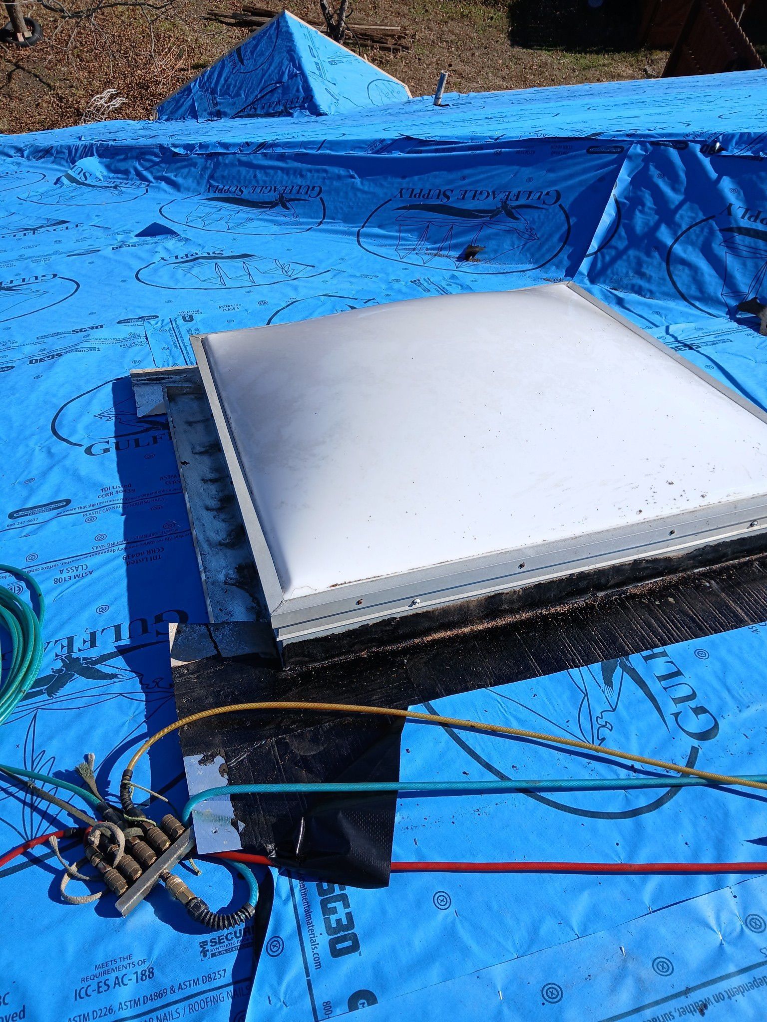 A skylight is sitting on top of a blue tarp.