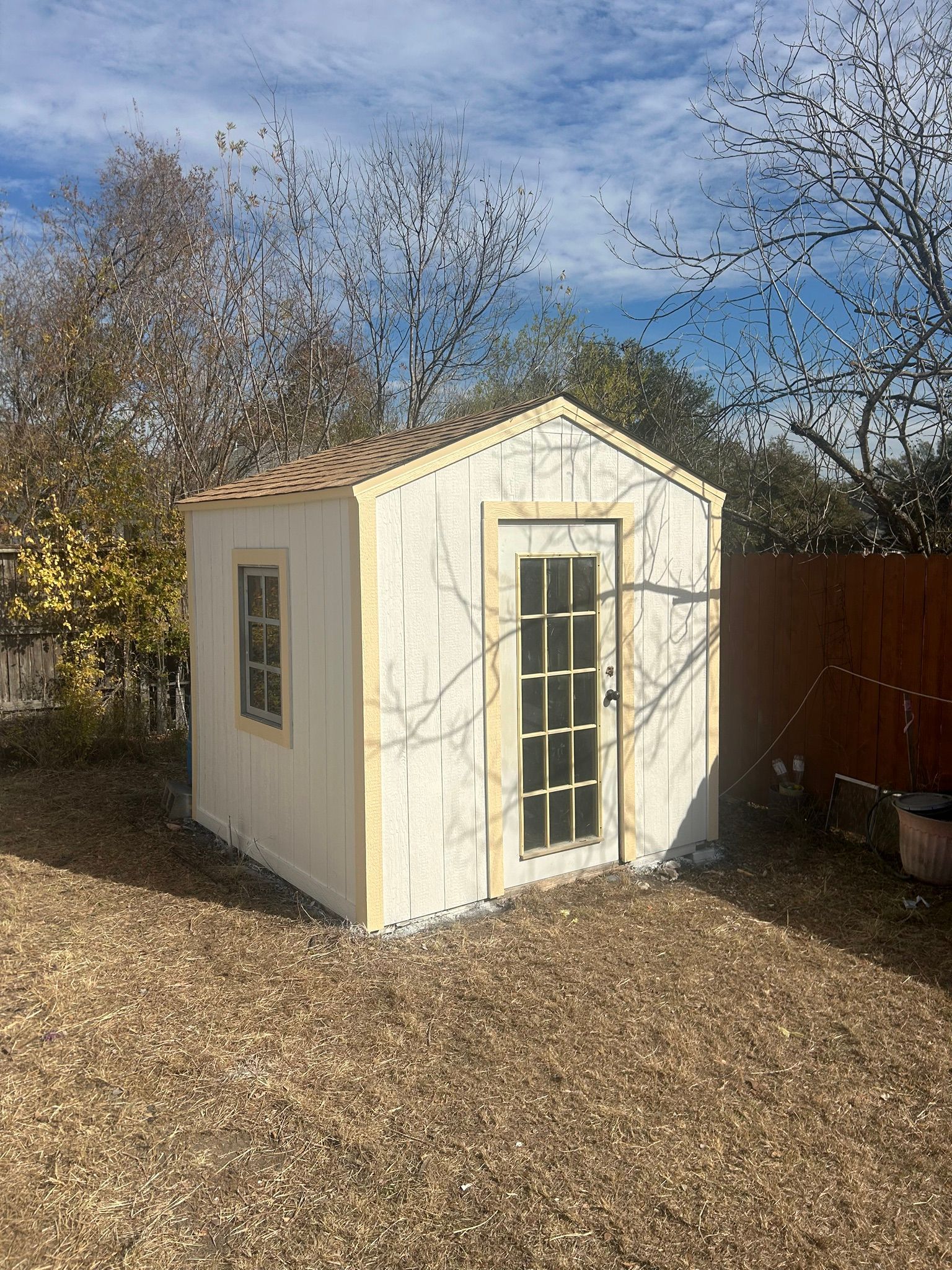 A small white shed with a door and windows in a backyard.