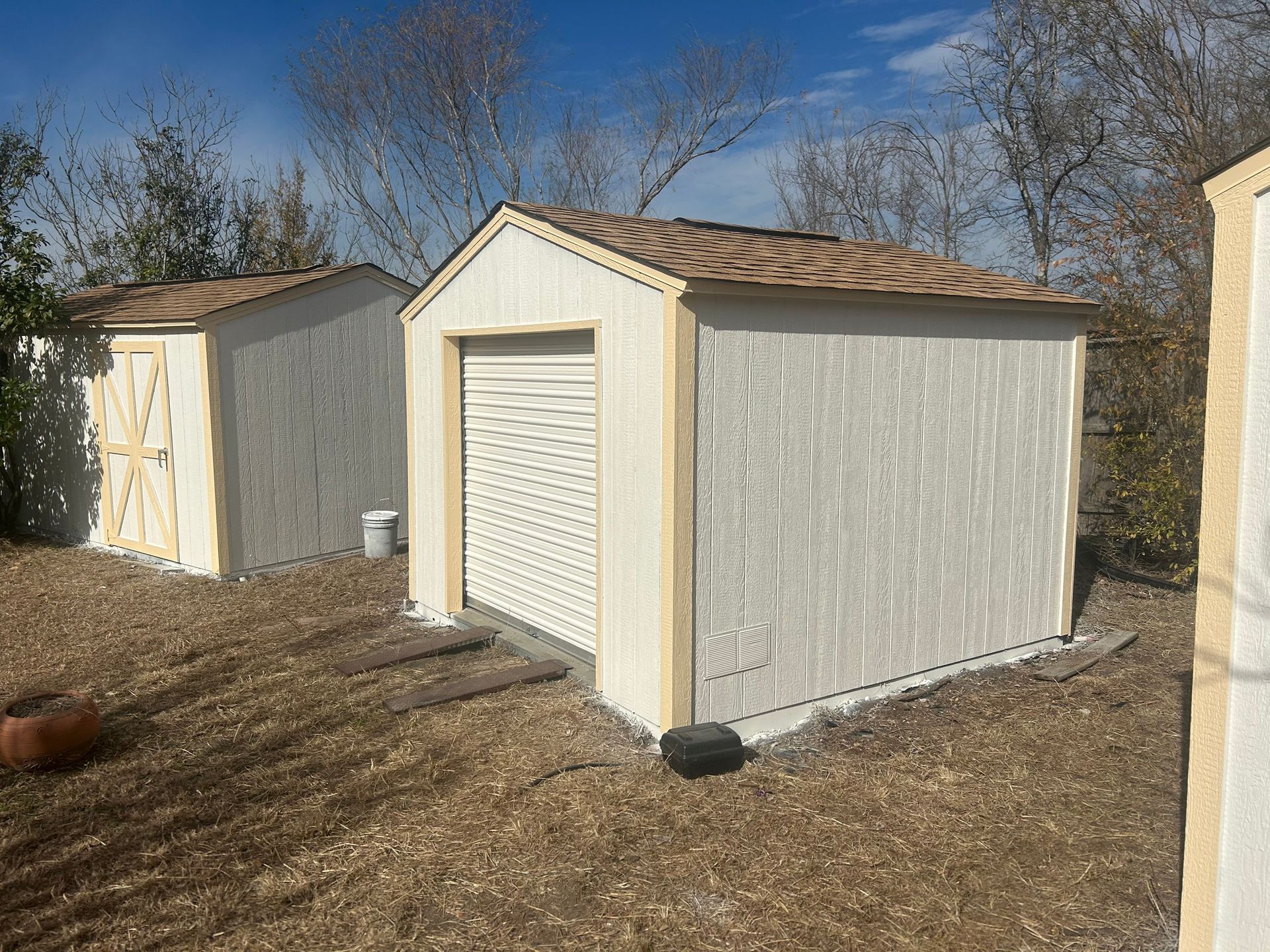 Two sheds are sitting next to each other in a dirt field.