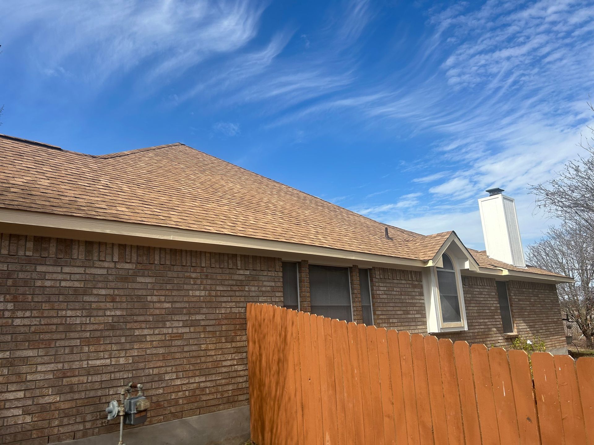 A brick house with a brown roof and a wooden fence in front of it.