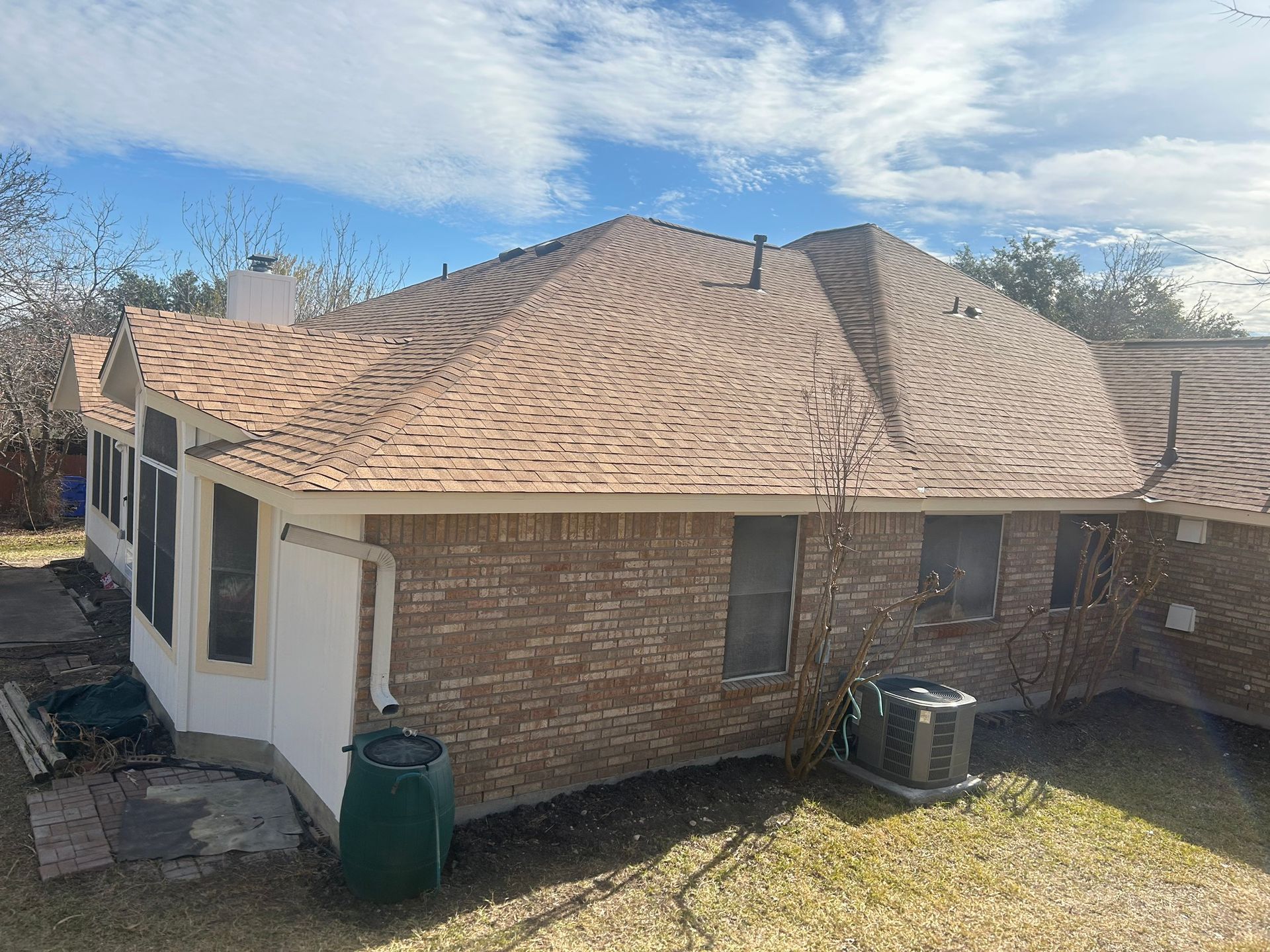 A brick house with a new roof and air conditioner in the backyard.
