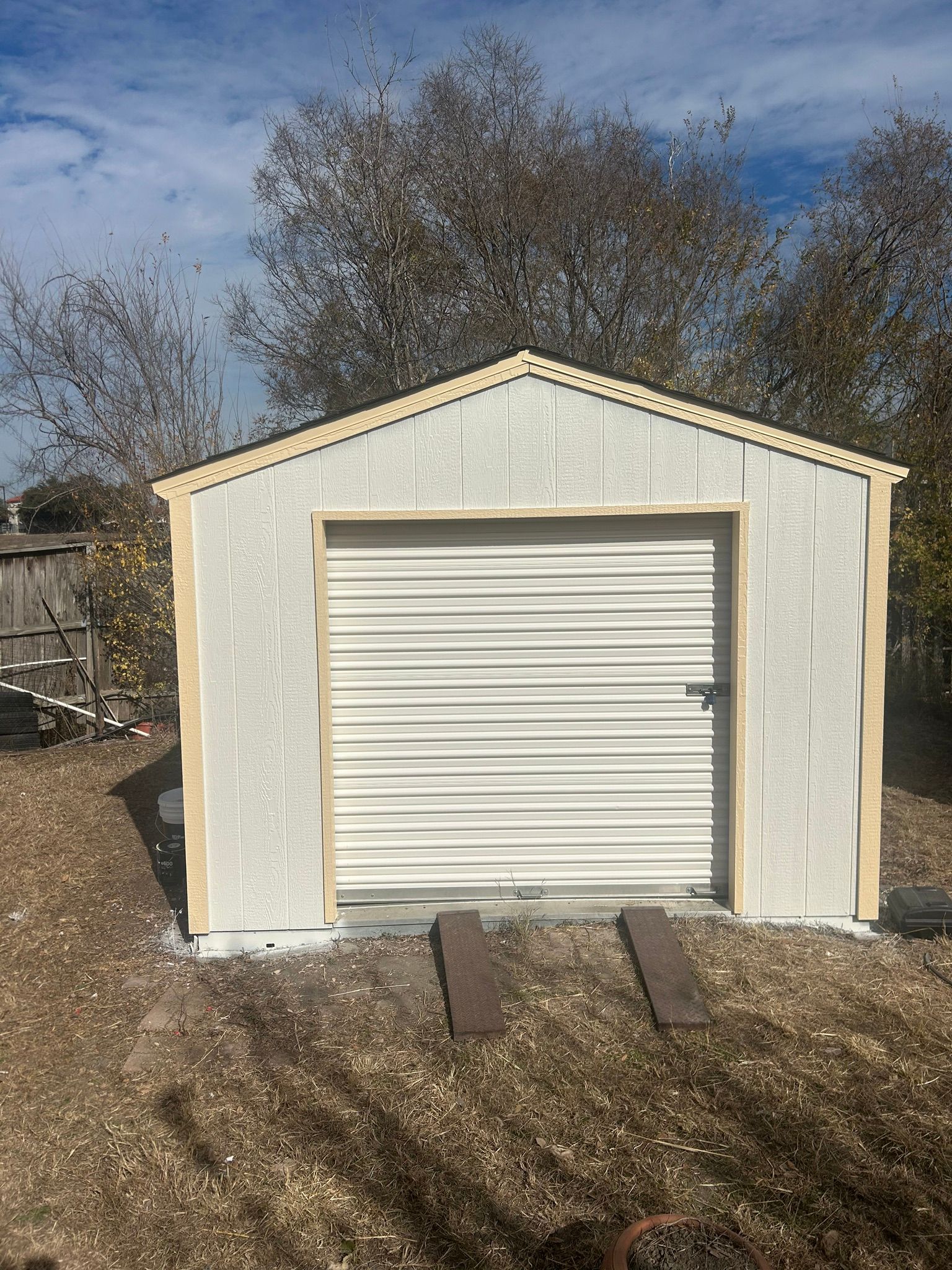 A white garage with a white door is sitting in the middle of a dirt field.
