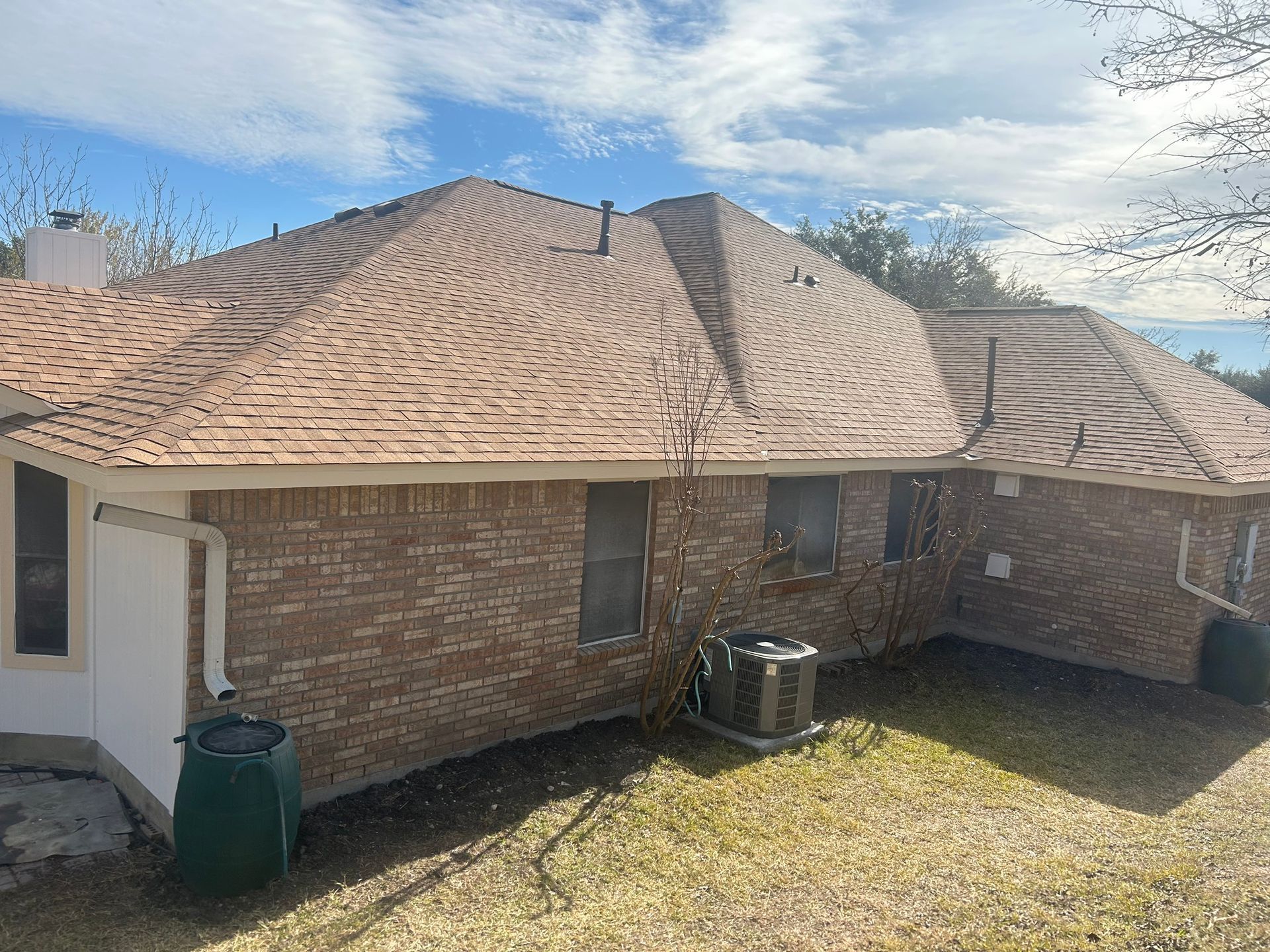 A brick house with a new roof and air conditioner in the backyard.