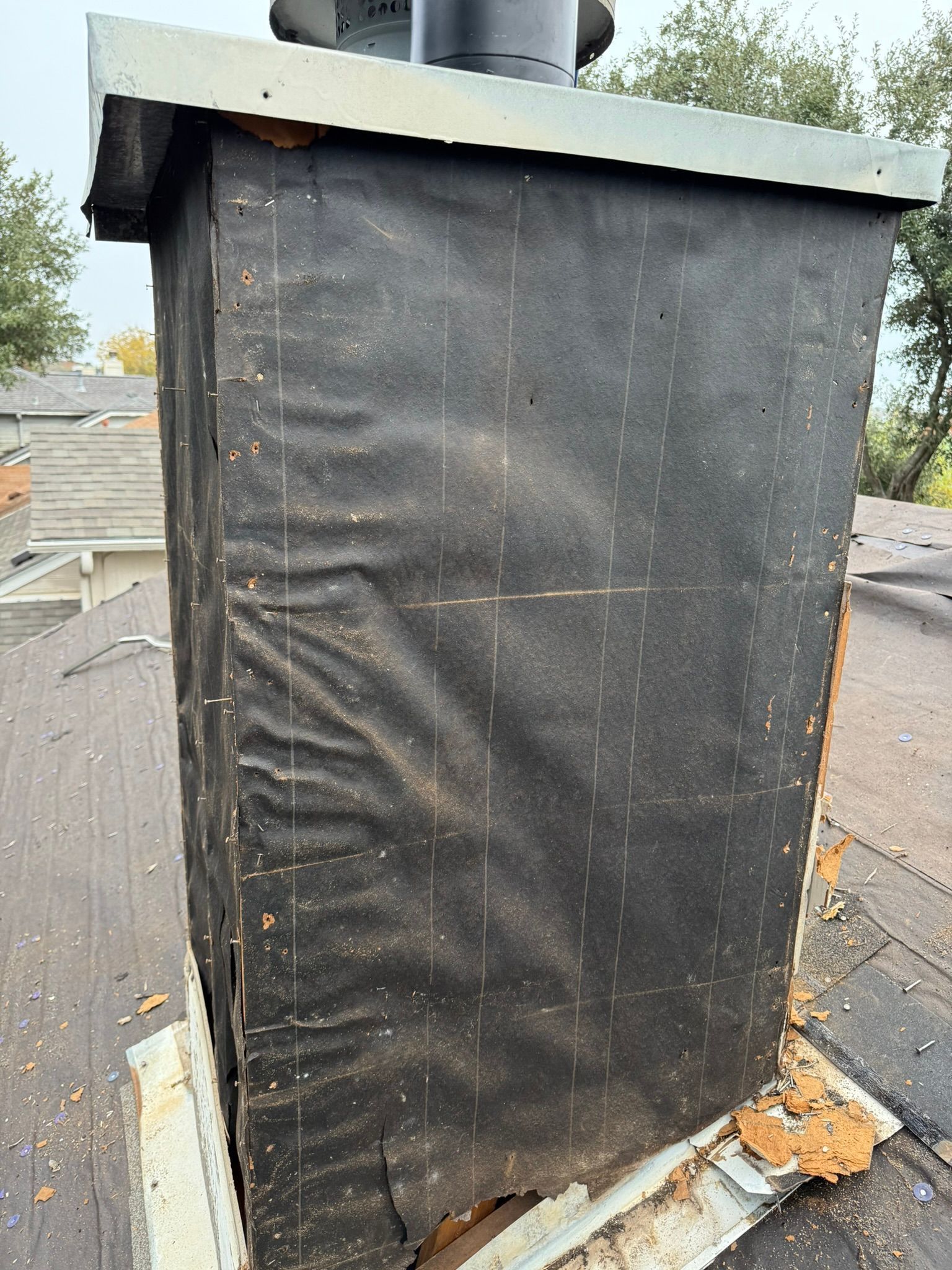 A chimney on top of a roof with a black tarp on it.