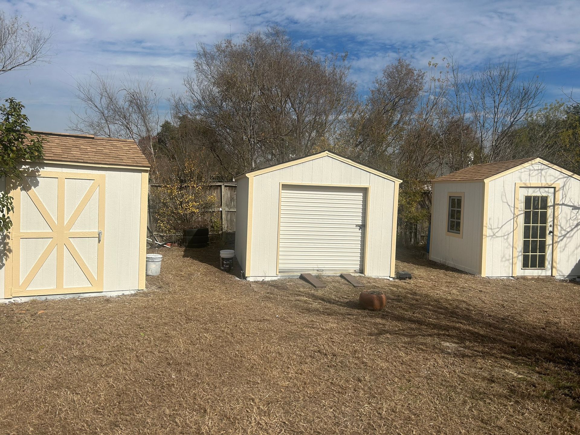 Three white sheds are sitting next to each other in a dirt yard.