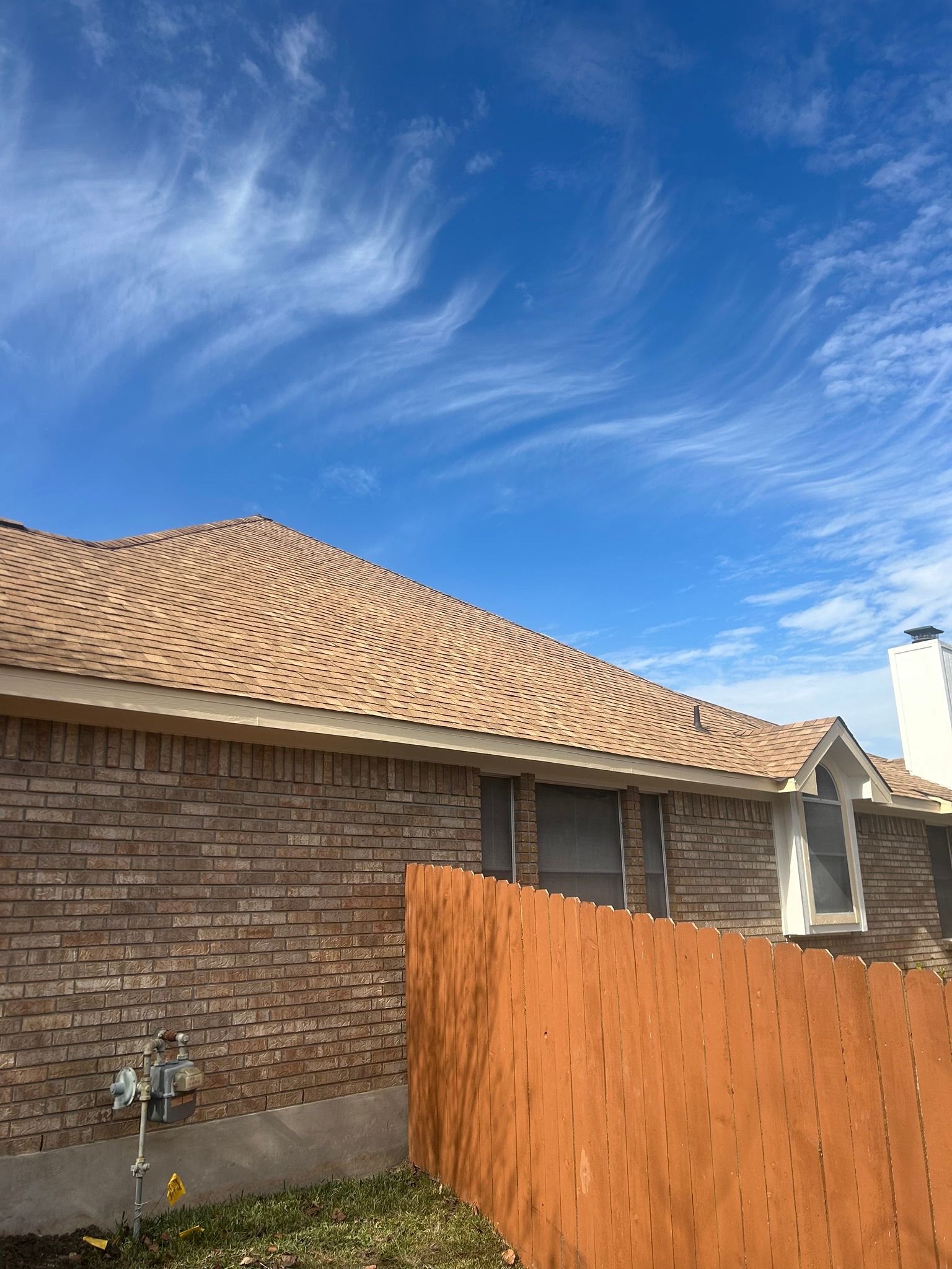 A brick house with a roof and a wooden fence in front of it.