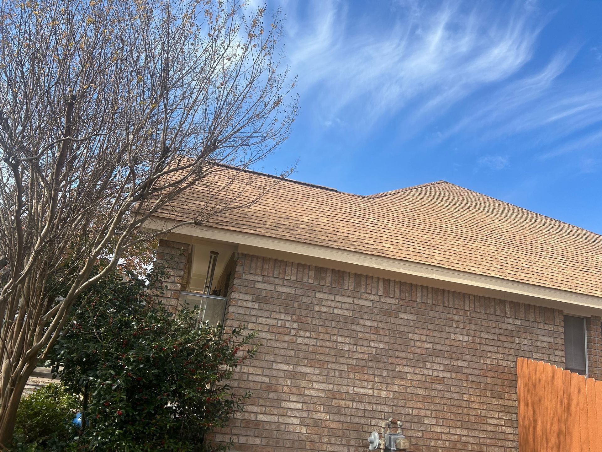 A brick house with a tan roof and a blue sky in the background.