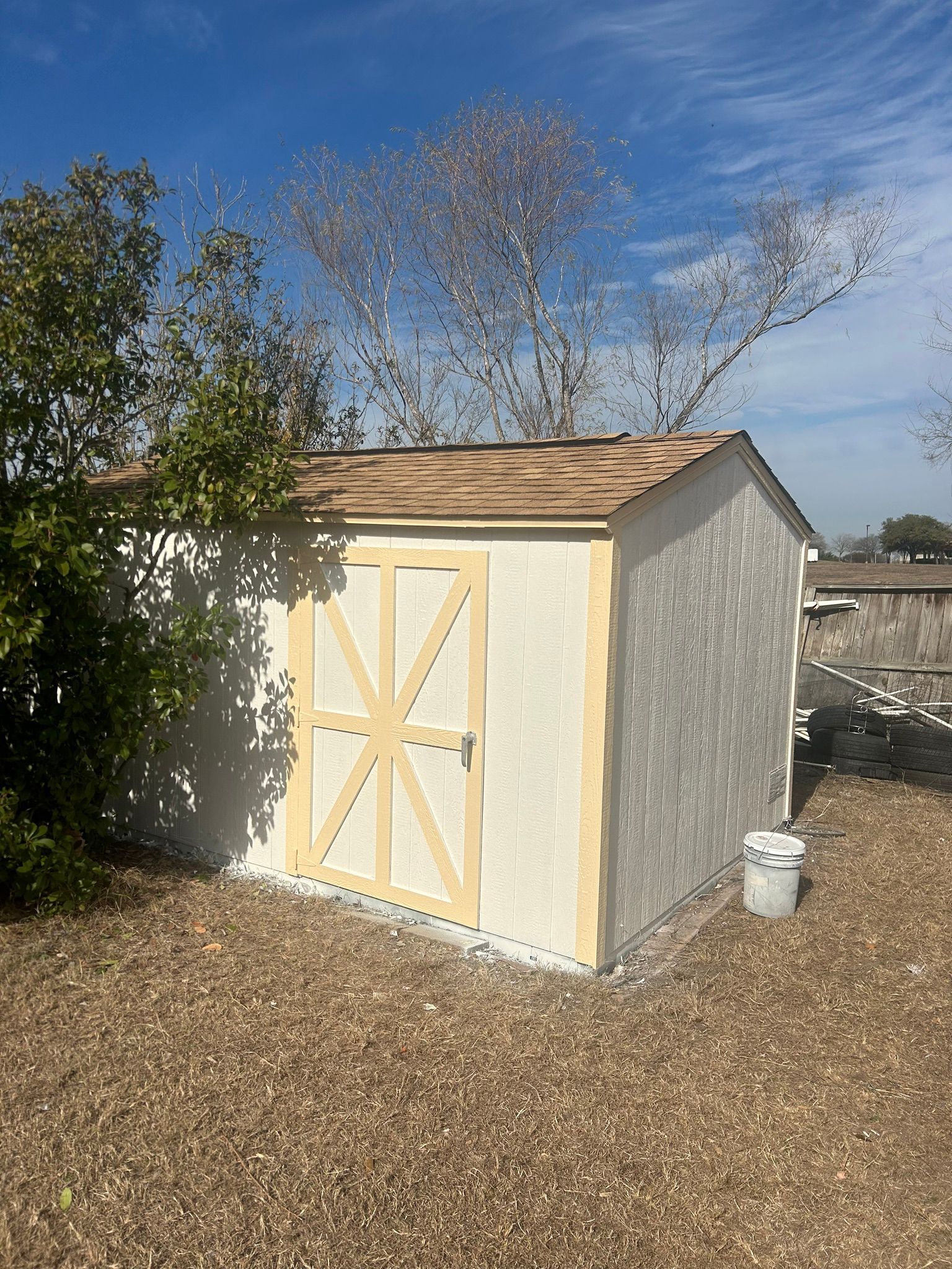 A small white shed with a wooden roof is sitting on top of a gravel lot.