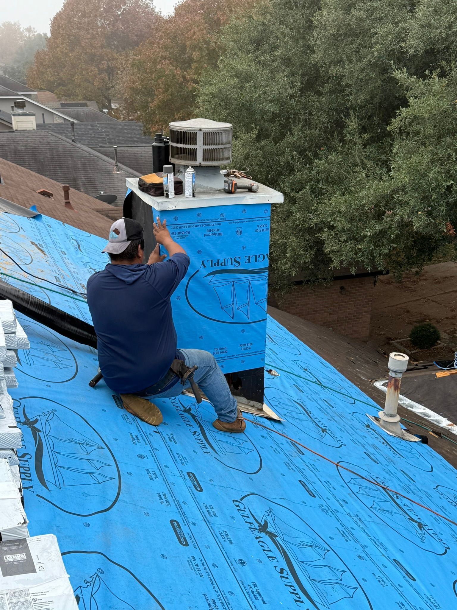 A man is sitting on top of a roof working on a chimney.