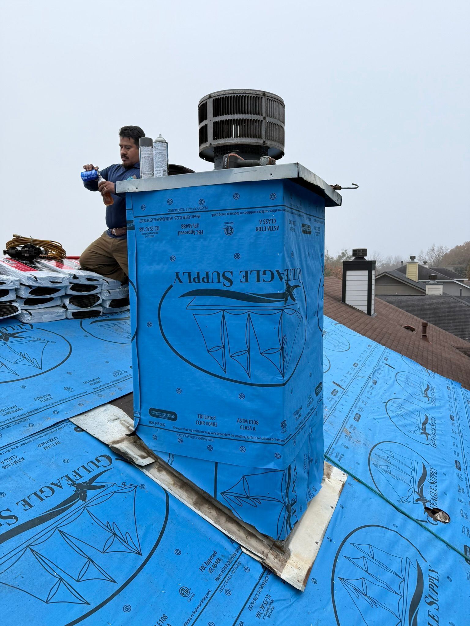 A man is sitting on top of a blue tarp on a roof.