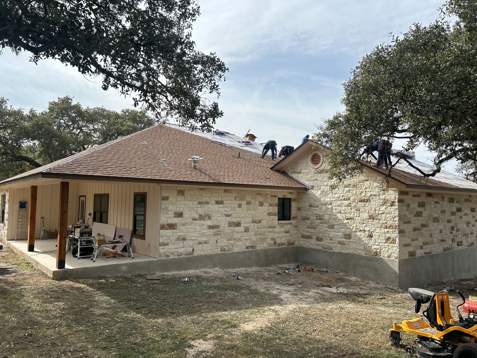 A house with a roof that is being built and a lawn mower in front of it.