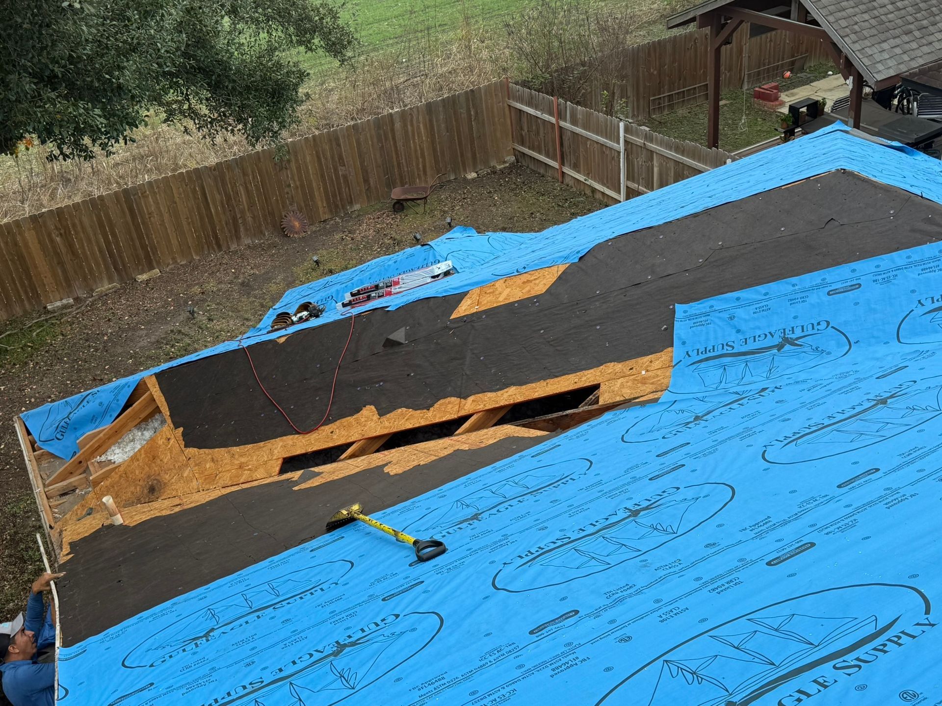 A man is working on a roof with a blue tarp on it.