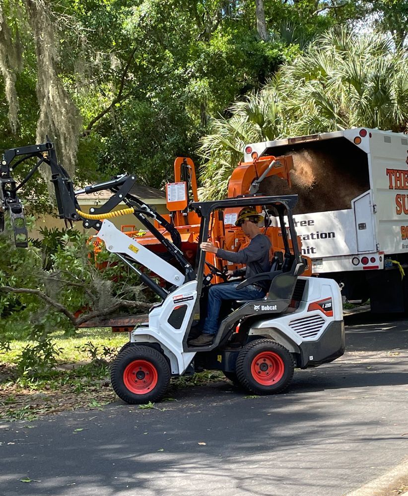 A man is driving a small tractor down a street next to a truck.