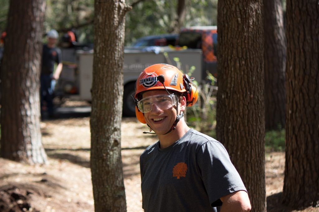 A man wearing a helmet and goggles is standing in the woods.