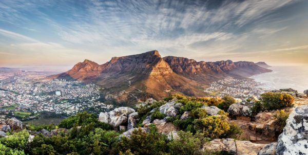 View of Cape Town, South Africa, with Table Mountain at sunset. City, ocean, and mountains are visible.
