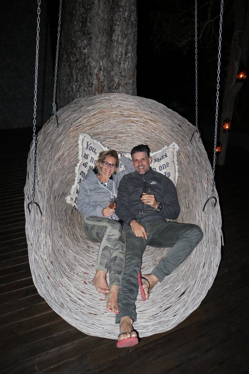 Couple sitting in a large woven swing at night. They are smiling, with an outdoor setting.