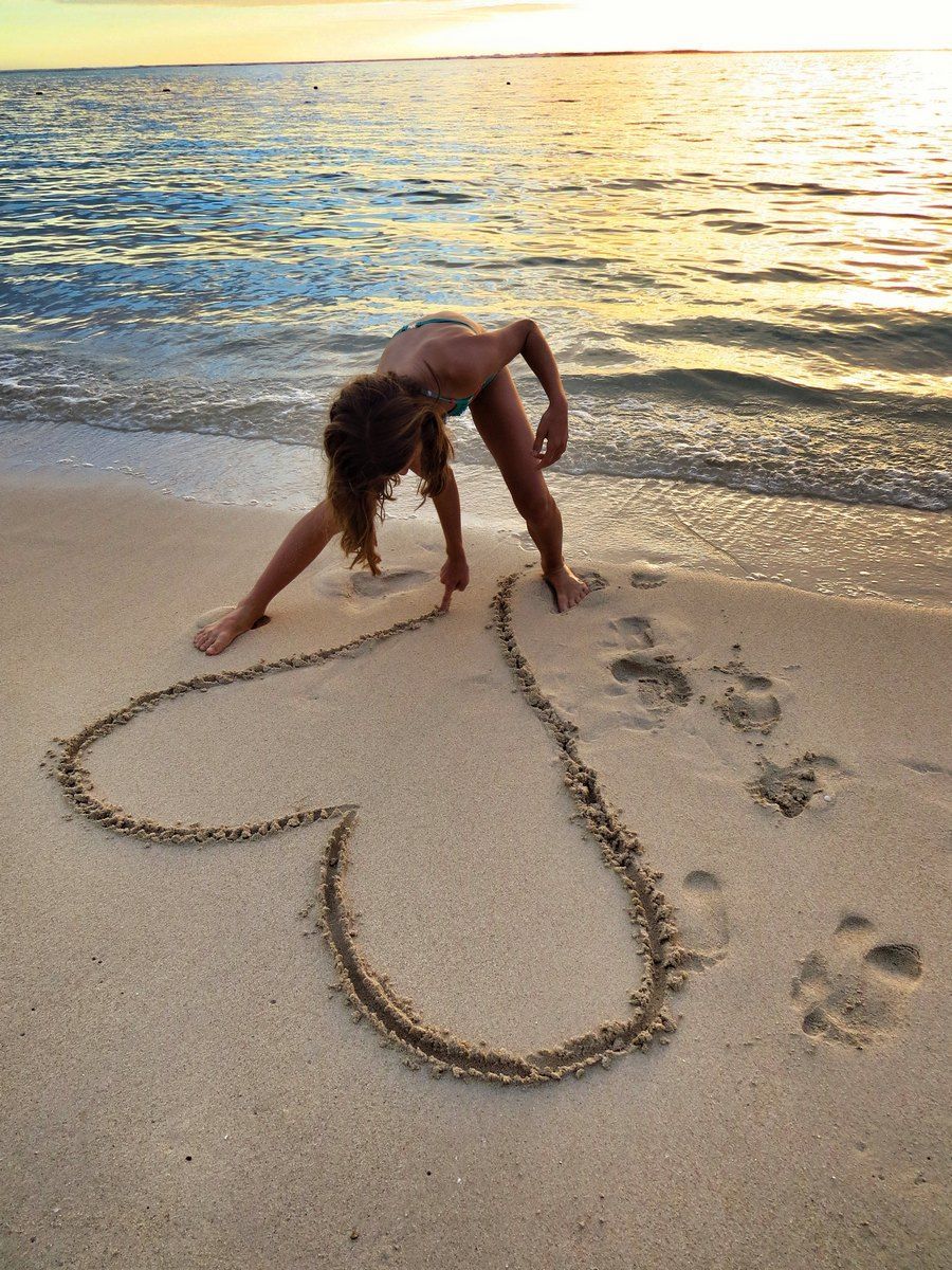 Girl drawing a heart in the sand on a beach at sunset.