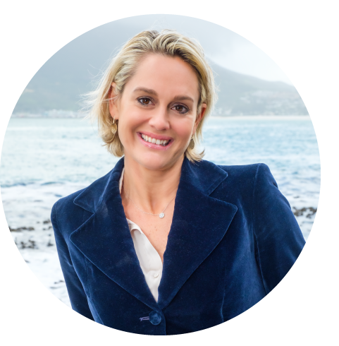Woman with blonde hair, smiling, wearing a navy blue blazer, standing near a body of water.