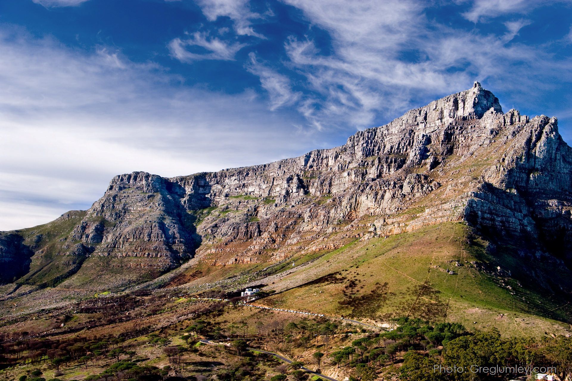 Table Mountain, South Africa, with flat top and rocky cliffs, under a blue sky with wispy clouds.
