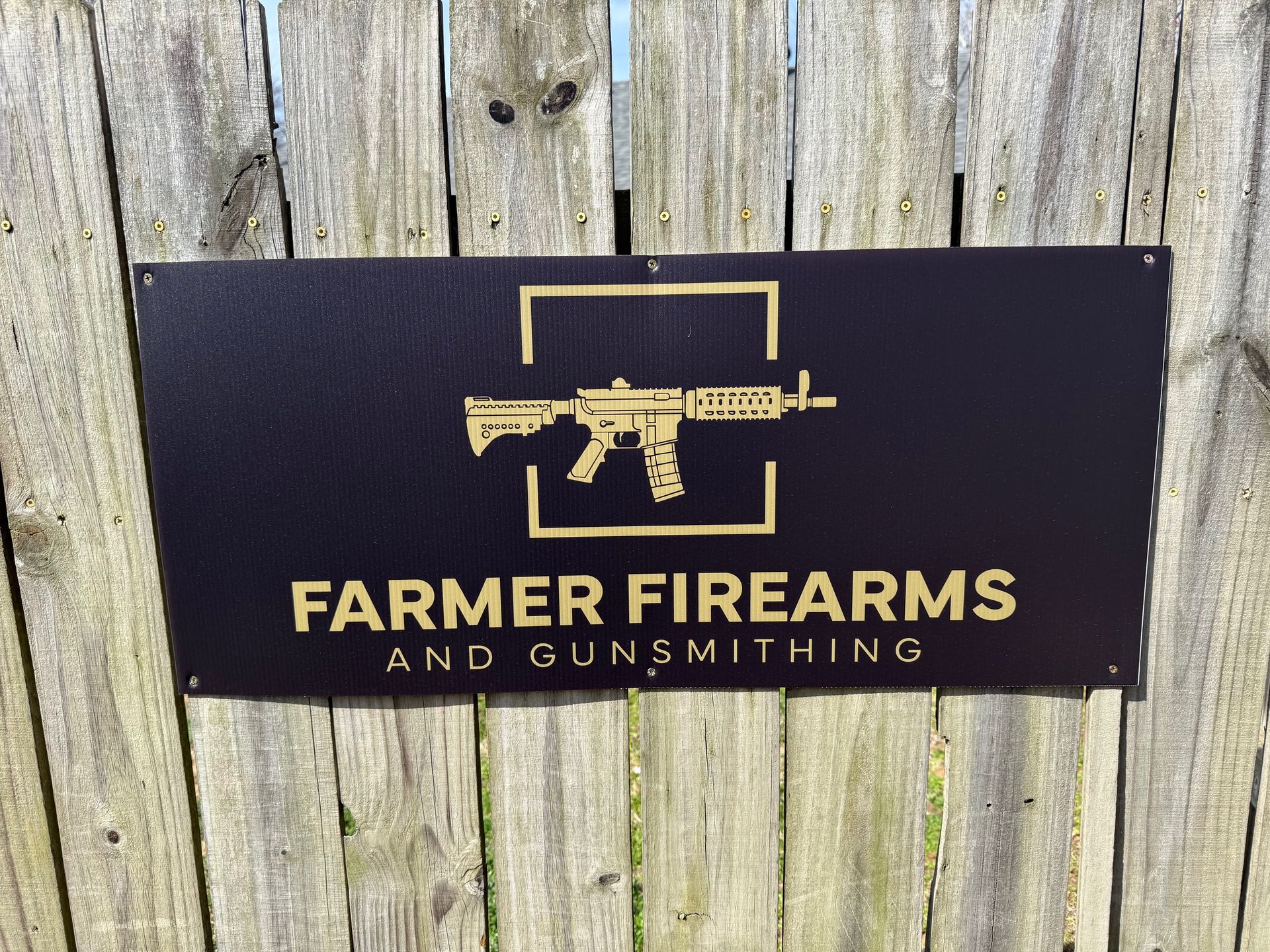 Farmer Firearms and Gunsmithing sign with gold text and gun graphic on a wooden fence