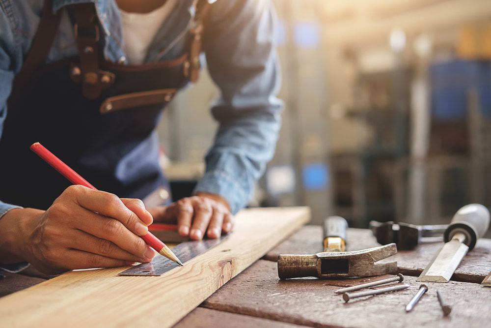A Man Is Measuring A Piece Of Wood With A Ruler And Pencil — Canyon Carpentry in Redridge, QLD