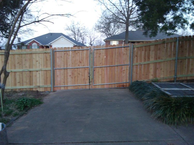 A wooden fence surrounds a driveway with a house in the background