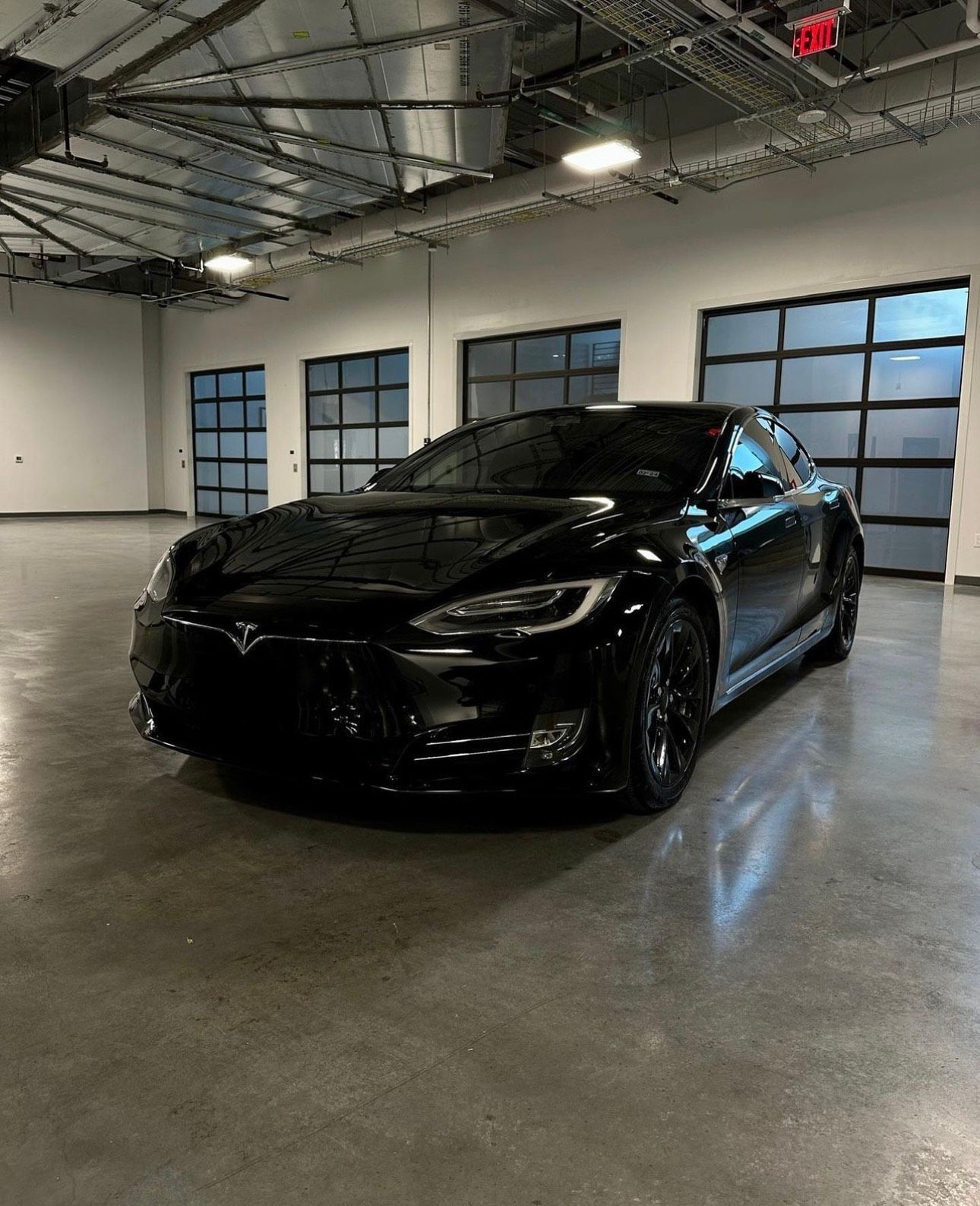 Black Tesla car parked inside a large room with garage doors.