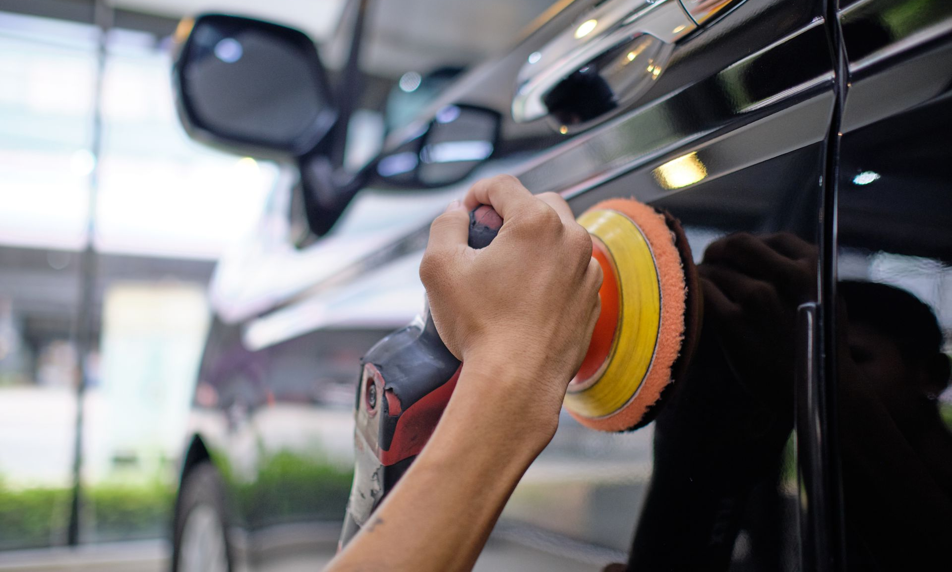 Hand polishing a black car with a red and yellow buffer pad