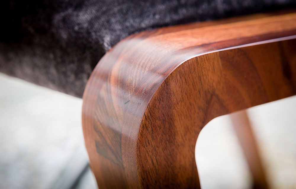 A close up of a designer wooden chair with a black cushion.