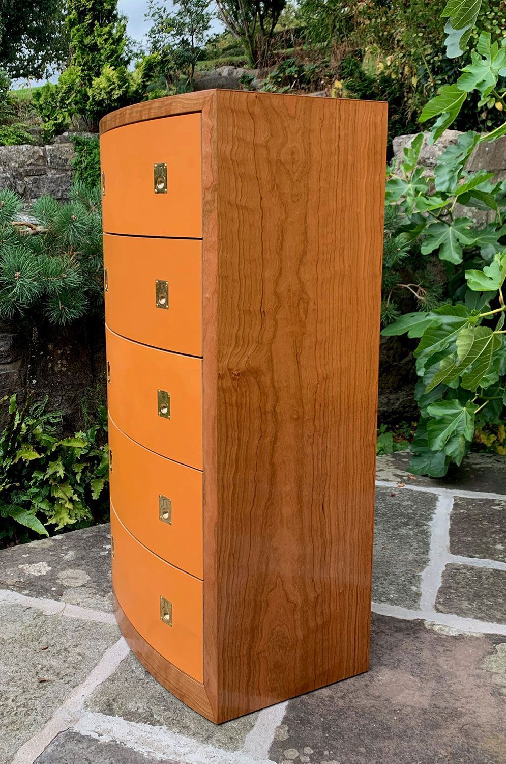 A designer wooden art cabinet with orange drawers is sitting on a stone patio.