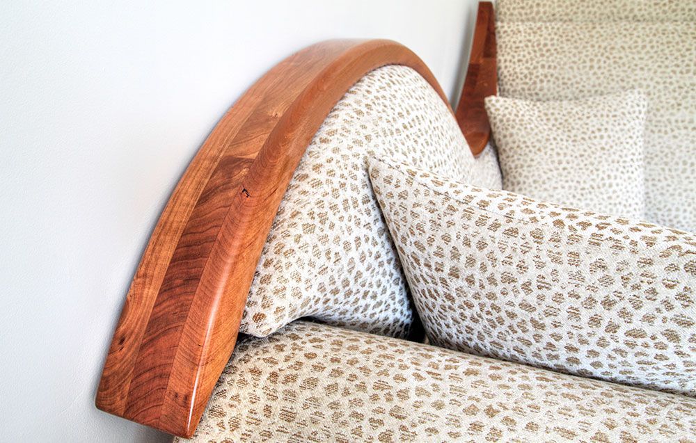 A close up of a designer handcrafted armchair with leopard print pillows and a wooden headboard.