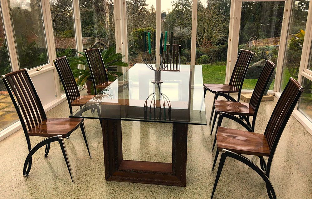 A handcrafted table base with glass table top and tailored chairs in a room with a lot of windows