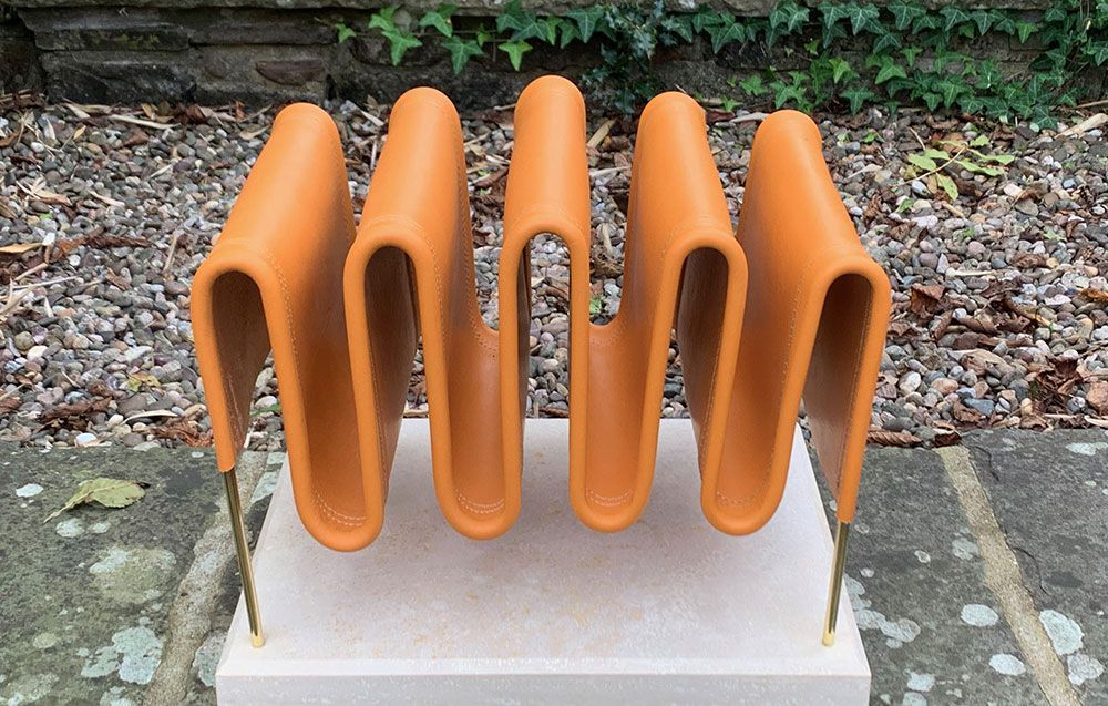 A sculpture of orange leather sitting on top of a oak base to create a bespoke magazine rack.