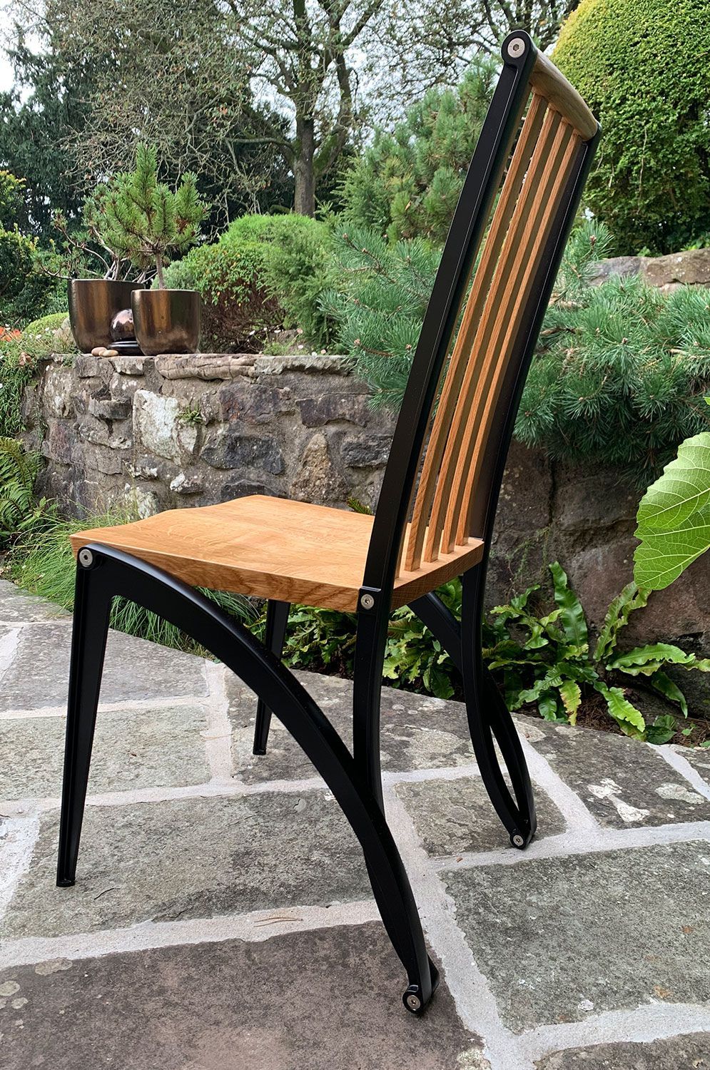 Mantide, a popular designer wooden chair is sitting on a stone patio next to a stone wall.