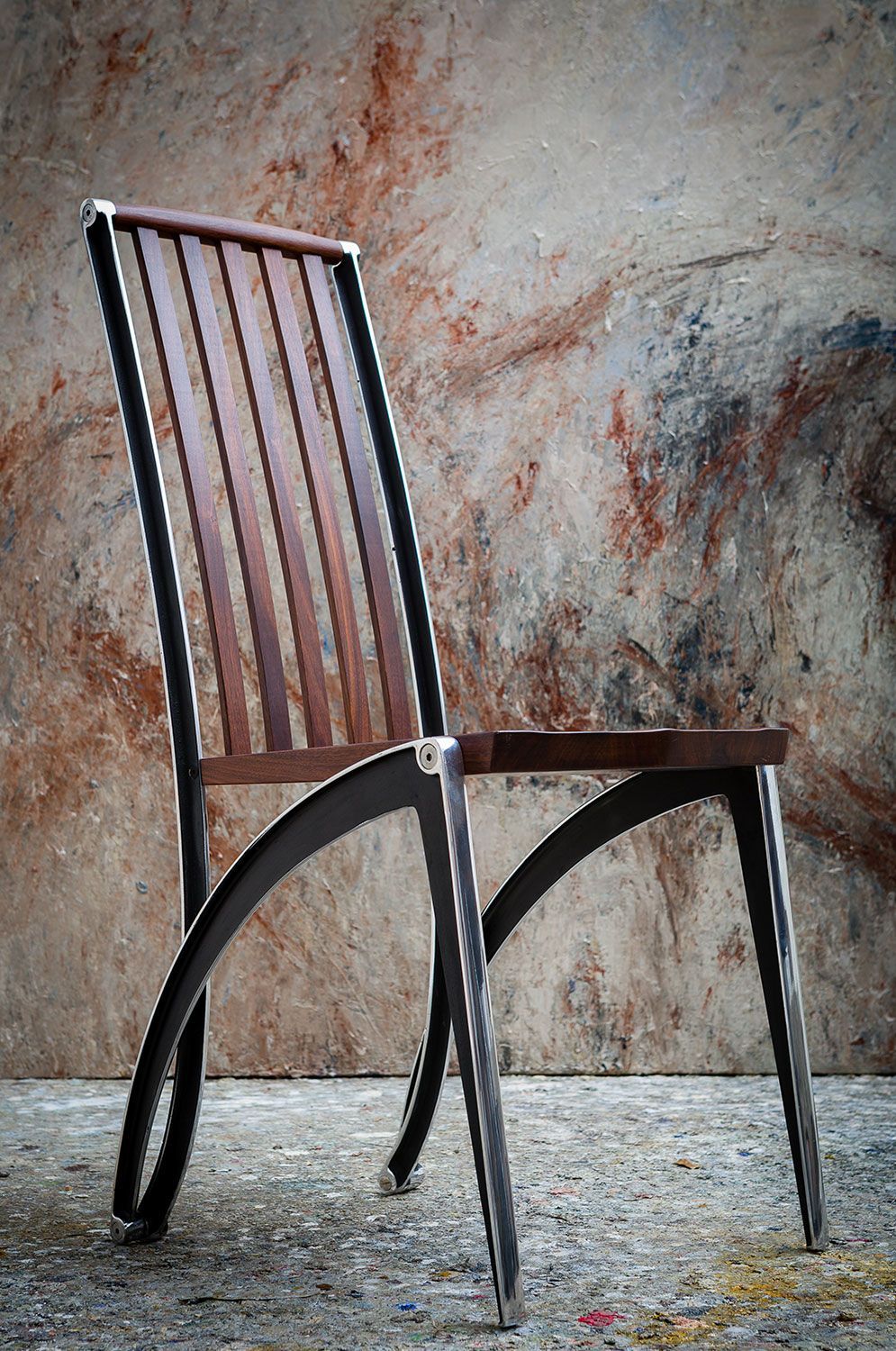 A handcrafted wooden chair with metal legs is sitting in front of a wall.