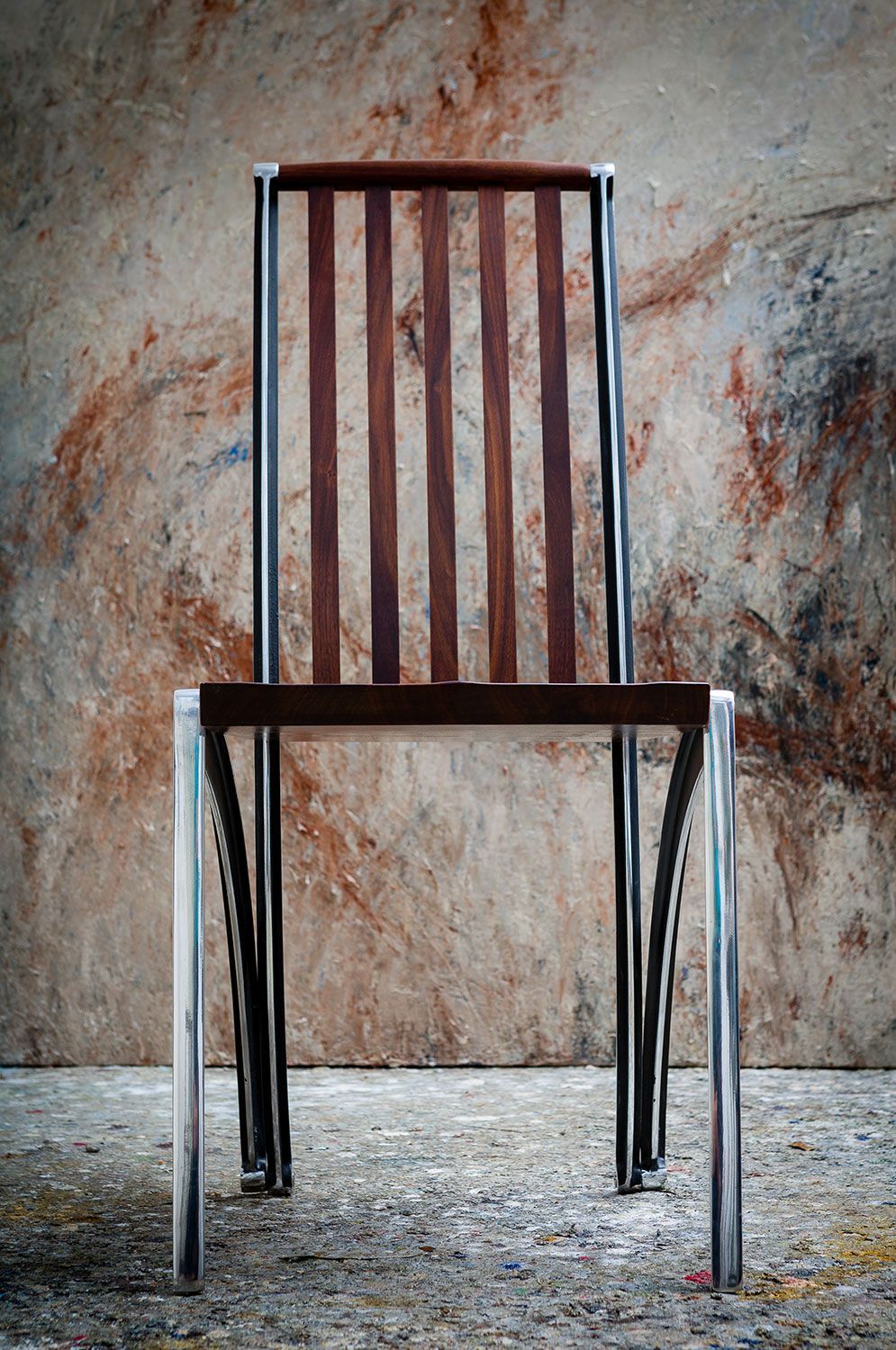 A designer walnut chair with metal legs is sitting in front of a wall.