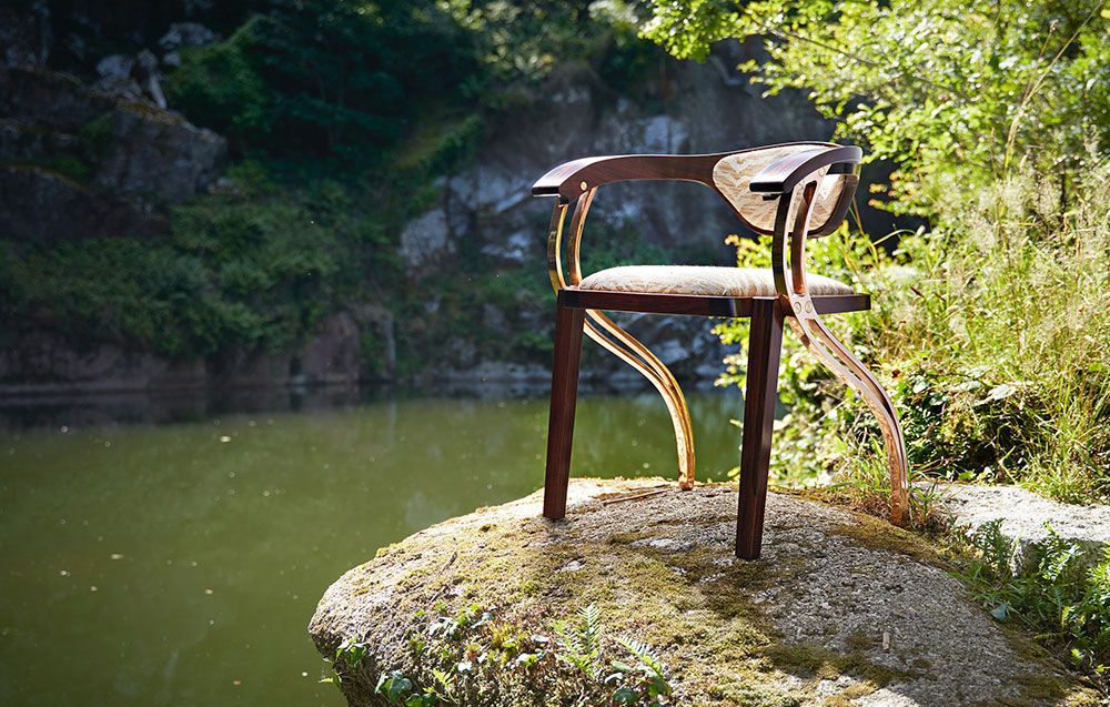 A designer dining chair is sitting on a rock near a lake.