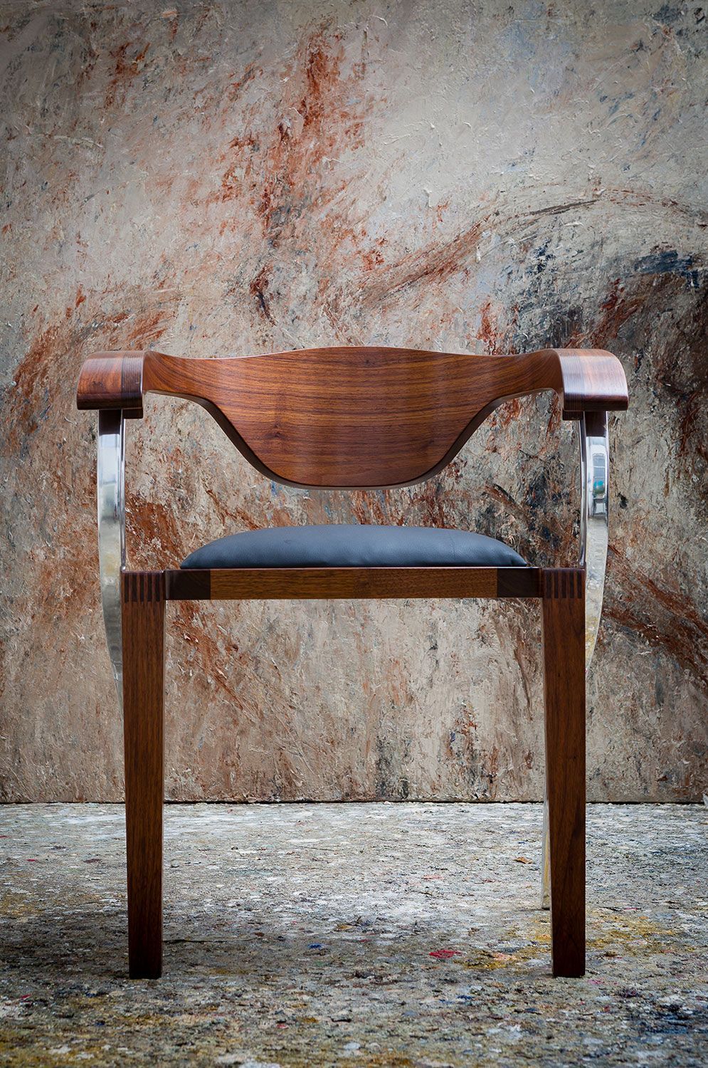 A luxury dining wooden chair is sitting in front of a concrete wall.