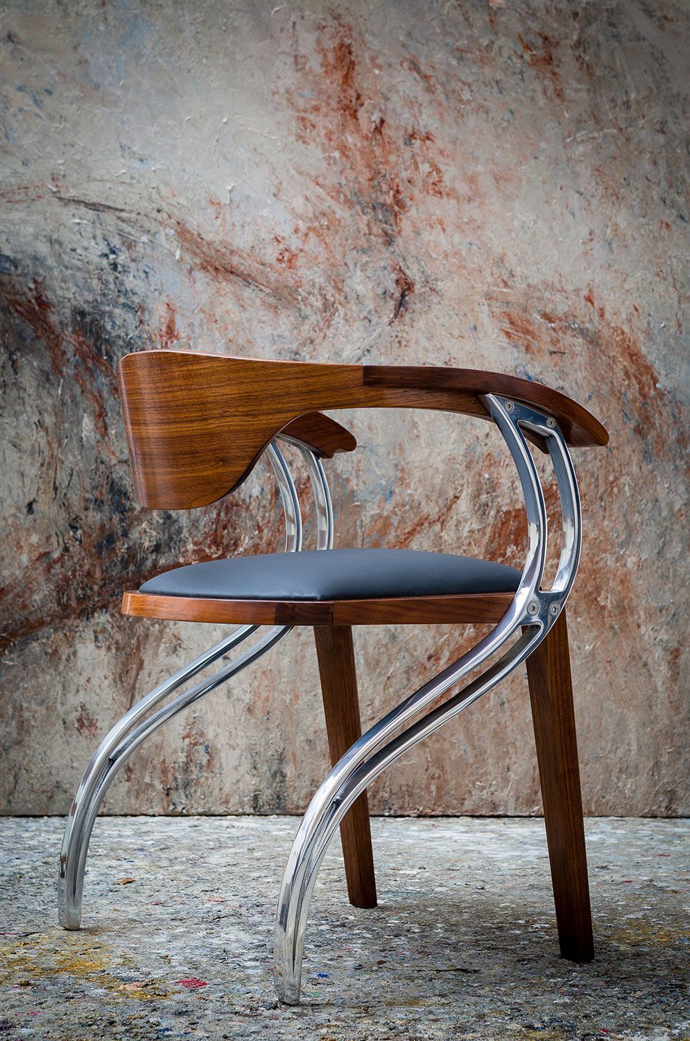 A wooden handcrafted chair with a metal frame is sitting in front of a wall.