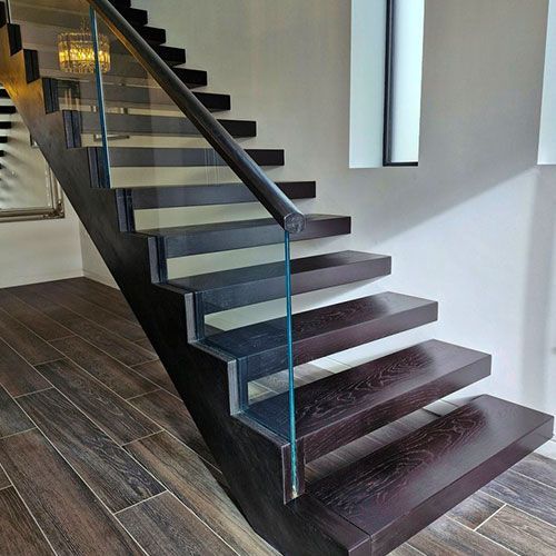 A fitted handcrafted wooden staircase with a glass railing in a room.