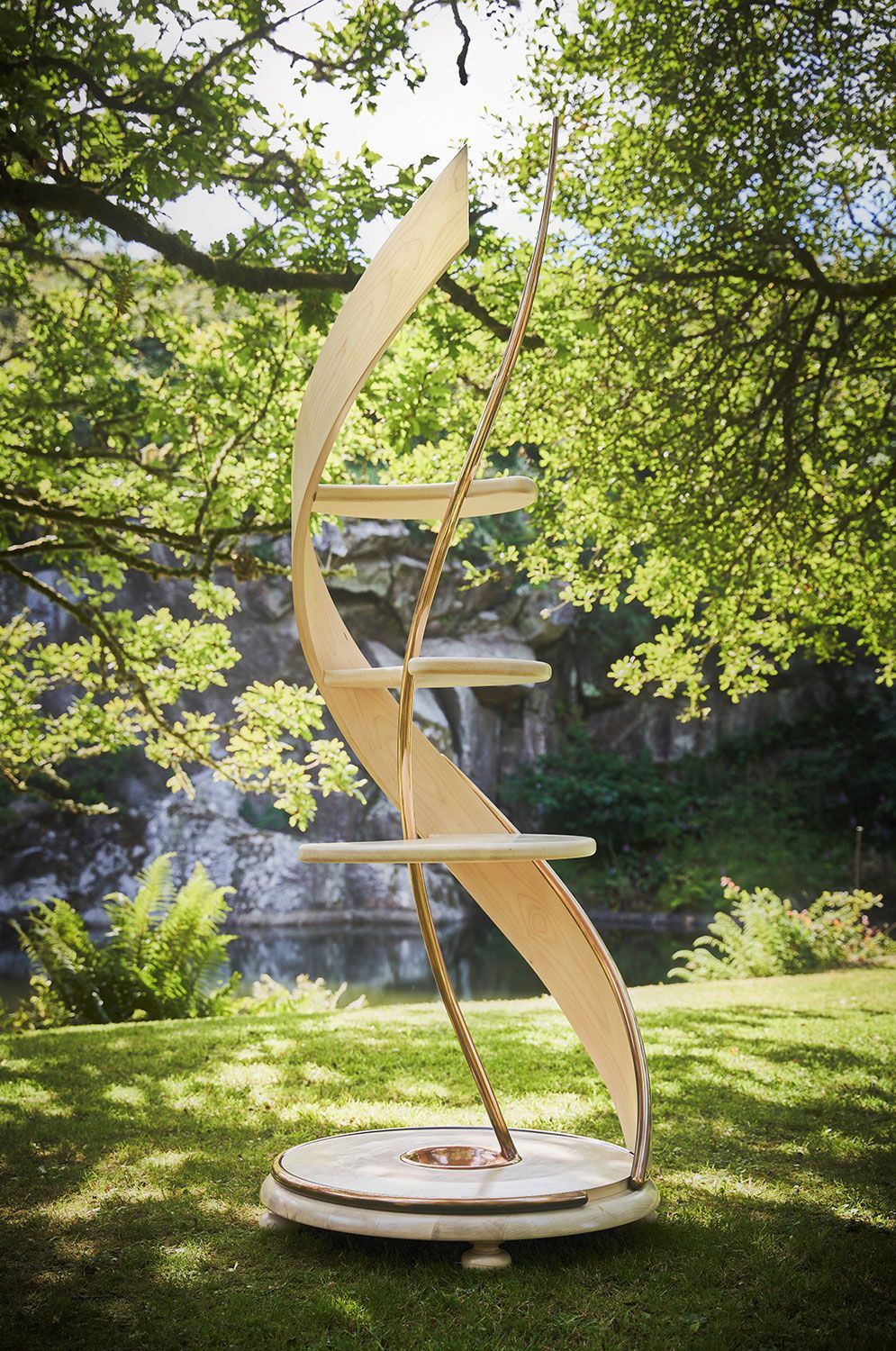 A handcrafted sycamore sculpture in the shape of a dna is sitting on top of a lush green field.