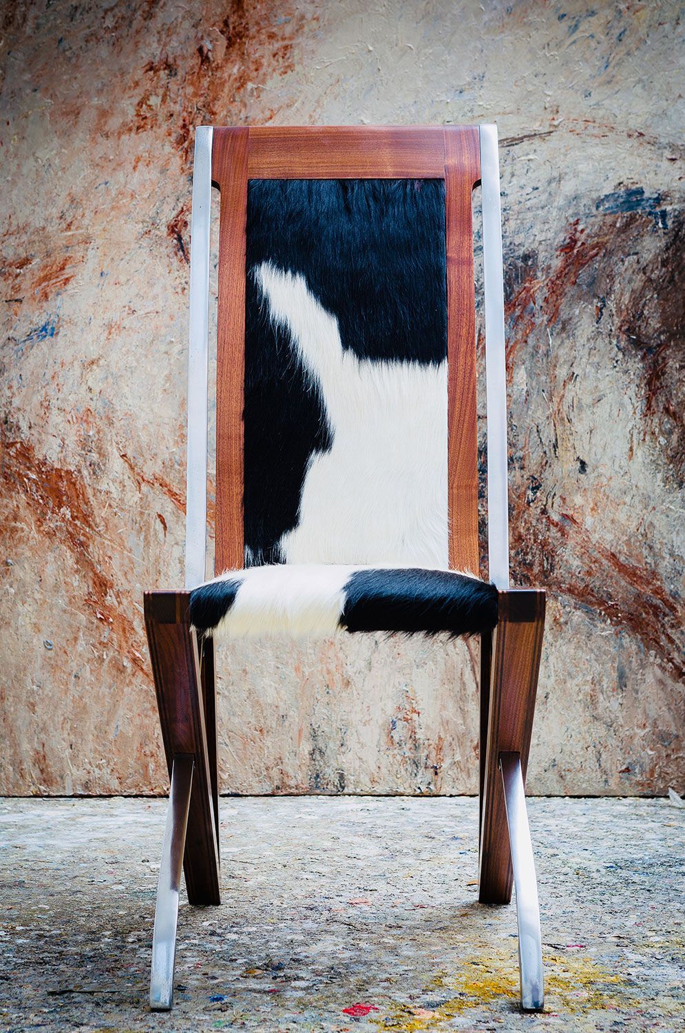 A designer wooden chair with a black and white cowhide seat crafted by sebastian blakeley