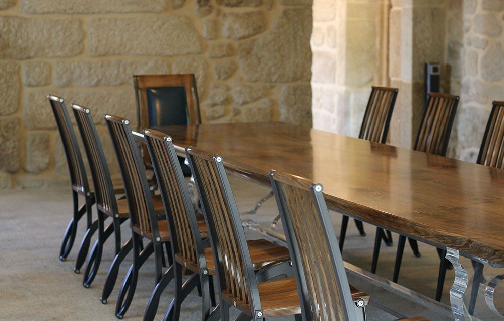 A long hand crafted walnut dining table with chairs in front of a stone wall