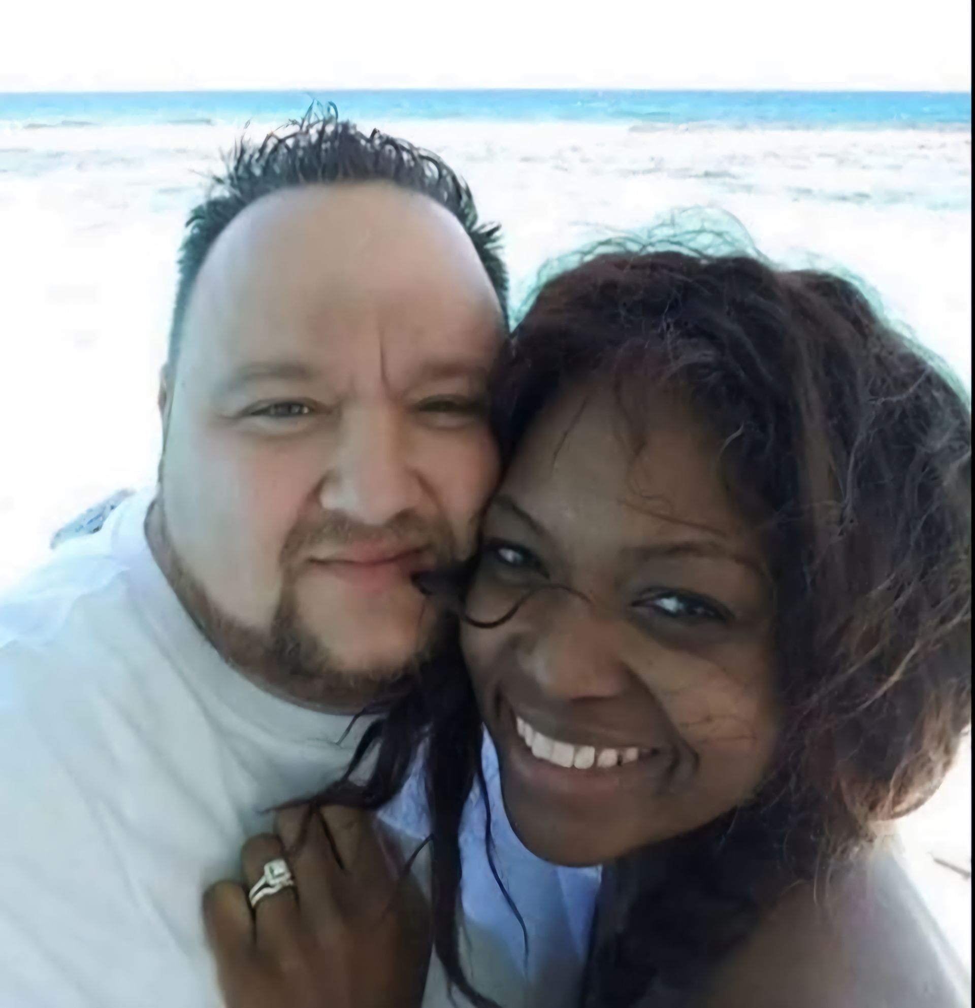 A man and a woman are posing for a picture on the beach.