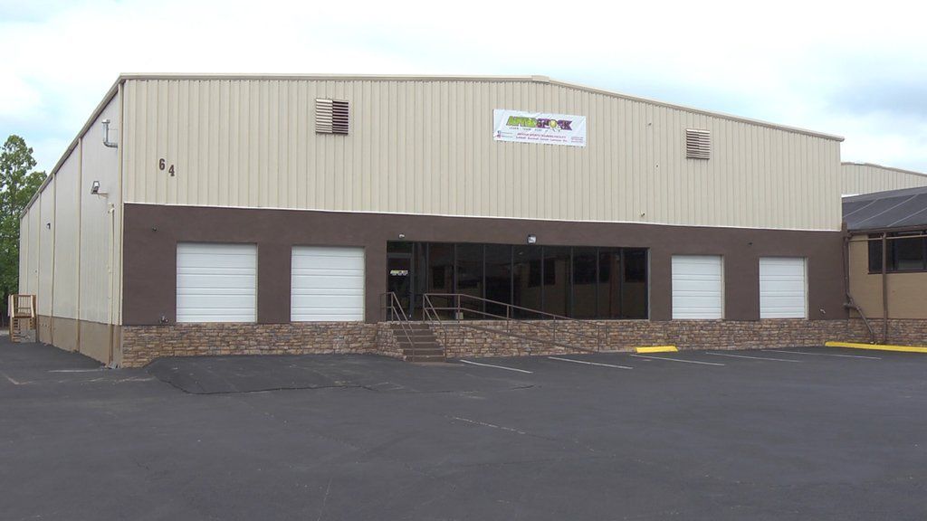 Beige and brown warehouse building with open entrance, loading dock, and parking area.