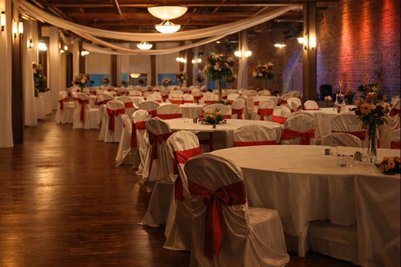 Wedding reception hall with round tables covered in white linens and red chair sashes.